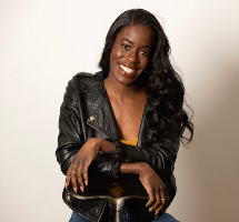 Allison Edwards-Crewe smiling in a leather jacket, sitting with hands crossed over the top of a backwards-facing chair